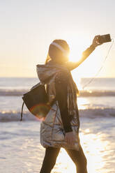 Mid erwachsene Frau, die Selfie mit Smartphone gegen Meer während Sonnenuntergang - JRVF00086