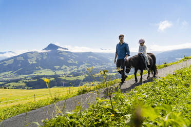 Vater geht neben seiner kleinen Tochter, die auf einem Pony reitet, einen alpinen Wanderweg entlang - DIGF13937