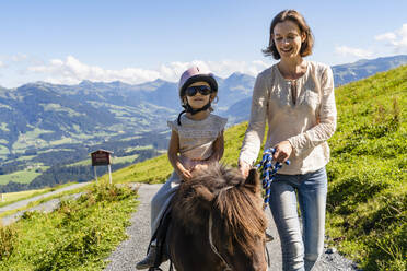 Mutter geht neben ihrer kleinen Tochter, die auf einem Pony reitet, einen alpinen Wanderweg entlang - DIGF13940