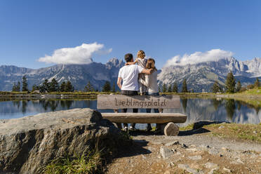 Family with one little daughter standing together behind lakeshore bench in Kaiser Mountains - DIGF13943
