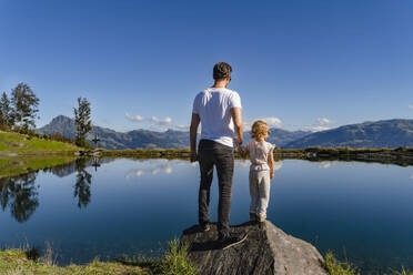 Father standing with little daughter on top of lakeshore boulder - DIGF13948