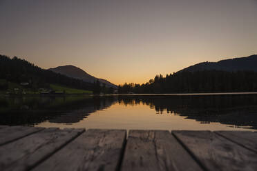 Berge, die sich in der Dämmerung im See spiegeln, mit dem Rand des Stegs im Vordergrund - DIGF13958