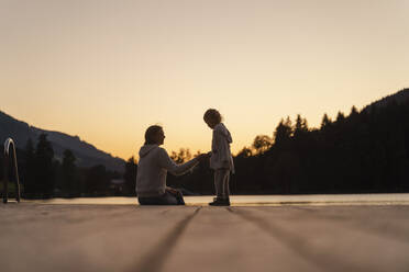 Mother talking with little daughter at end of lakeshore jetty at dusk - DIGF13961