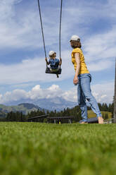 Mother and little daughter playing on swing - DIGF13972