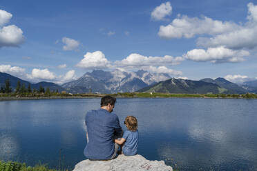 Vater und kleine Tochter sitzen zusammen auf einem Felsen am Seeufer - DIGF13978