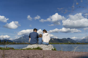 Familie mit kleiner Tochter sitzt zusammen auf einem Felsen am Seeufer - DIGF13980