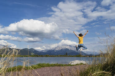 Junge Frau springt am Ufer eines Bergsees im Frühling - DIGF13984