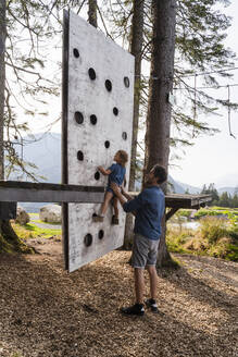 Vater hilft seiner kleinen Tochter beim Klettern an einer kleinen Waldkletterwand - DIGF13989