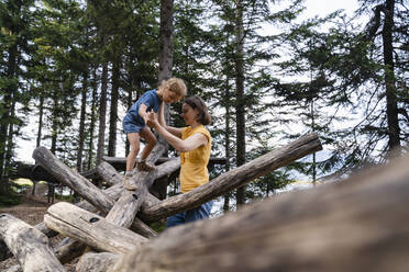 Mother assisting little daughter walking on top of wooden logs - DIGF13991