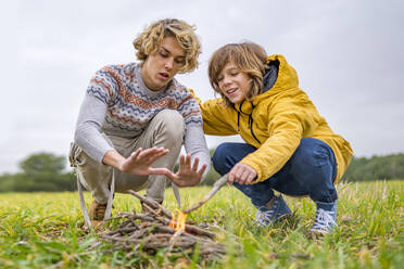 Zwei Brüder machen ein Lagerfeuer auf einer Wiese - GGGF00647