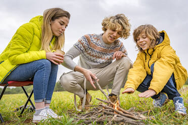 Drei Geschwister machen ein Lagerfeuer auf einer Wiese - GGGF00648