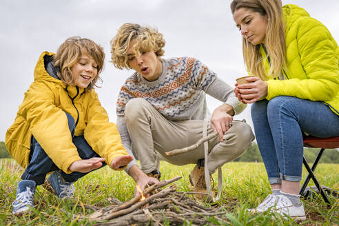 Drei Geschwister machen ein Lagerfeuer auf einer Wiese - GGGF00649