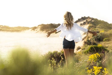 Carefree woman standing with arms outstretched at beach - SBOF02318