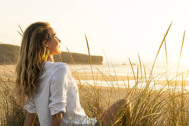 Woman looking at view while sitting on grass at beach - SBOF02326
