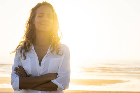 Woman standing with eyes crossed at beach during sunset stock photo