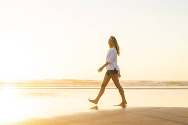 Glückliche Frau, die bei Sonnenuntergang am Strand spazieren geht - SBOF02332
