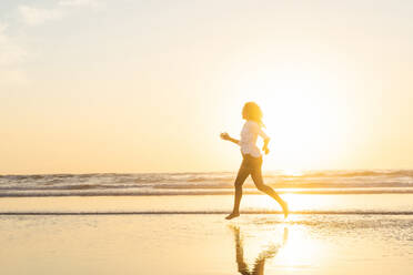 In silhouette of woman running in sea during sunset - SBOF02337