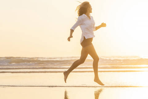 Frau schaut auf das Meer, während sie am Strand bei Sonnenuntergang läuft, lizenzfreies Stockfoto