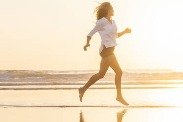 Woman looking at sea while running at beach during sunset - SBOF02338