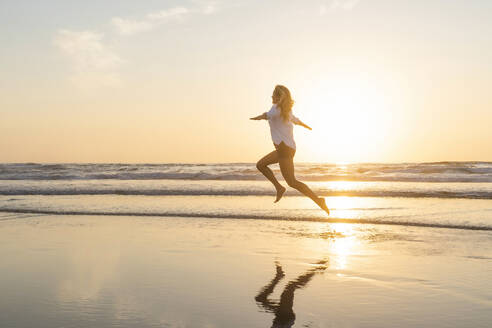 Happy woman with arms outstretched jumping against sea - SBOF02339