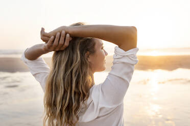 Carefree woman with hands behind head looking at view while standing against sea - SBOF02343