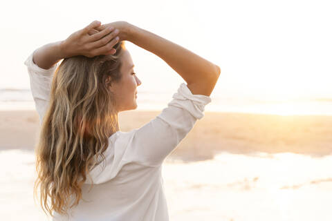 Woman with hands behind head standing at beach stock photo