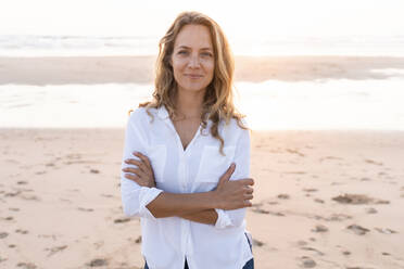 Smiling woman standing with arms crossed at beach - SBOF02347