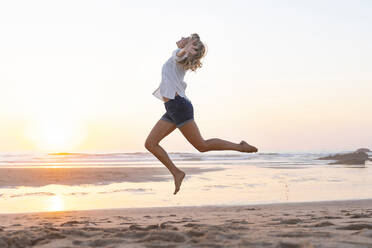 Carefree woman with arms outstretched jumping against sea during sunset - SBOF02349