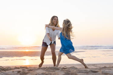 Mutter und Tochter genießen beim Spielen am Strand bei Sonnenuntergang - SBOF02350