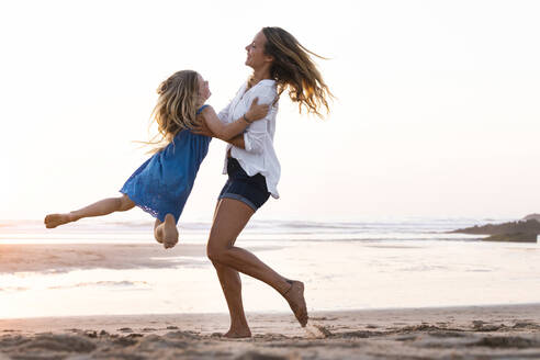 Mother carrying daughter while playing at beach - SBOF02351