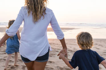 Mother with children running toward sea during sunset - SBOF02352