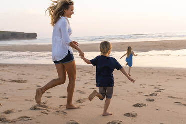 Cheerful mother running while playing with children at beach - SBOF02354