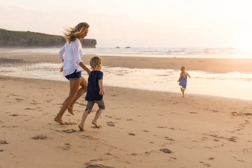 Mutter und Kinder genießen beim Laufen am Strand während des Sonnenuntergangs - SBOF02355