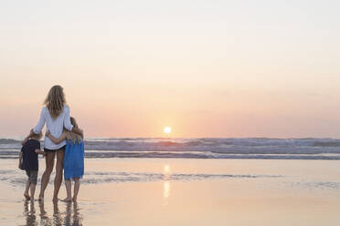 Mother embracing children while looking at view standing at beach - SBOF02360