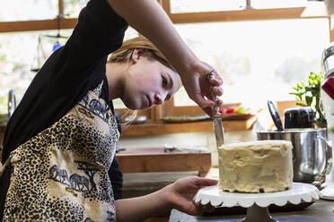 Teenager-Mädchen in der Küche beim Auftragen von Zuckerguss auf Kuchen - MINF15478