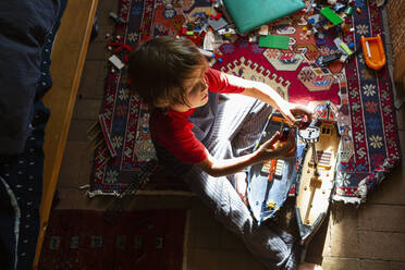 Draufsicht auf einen kleinen Jungen in seinem Zimmer, der mit seinen Spielsachen spielt - MINF15483