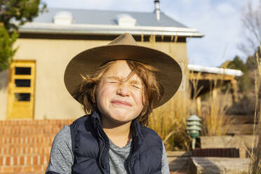 Portrait of young boy wearing fedora hat relaxing on his porch - MINF15492