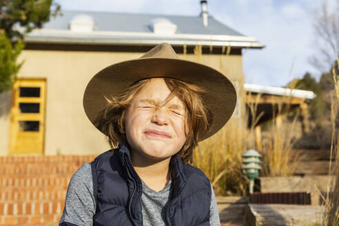 Porträt eines kleinen Jungen mit Filzhut, der sich auf seiner Veranda ausruht - MINF15492
