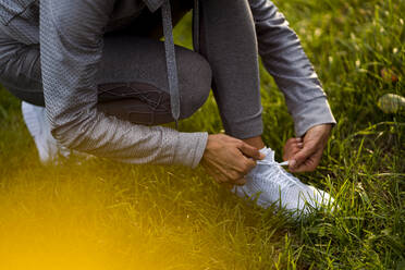 Sportswoman tying shoelace while crouching at park - MAUF03706