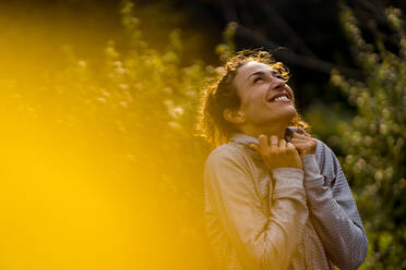 Happy sportswoman looking up while standing at park - MAUF03710