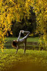 Female athlete stretching legs and hands while practicing yoga at park - MAUF03711