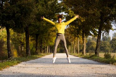 Weibliche Athletin mit ausgestreckten Armen, die beim Sport im Park springt - MAUF03715