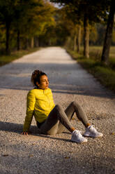 Weibliche Athletin ruht sich bei Sonnenuntergang auf der Straße sitzend aus - MAUF03721