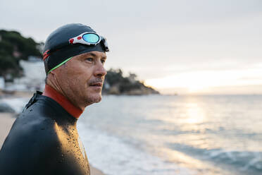 Porträt eines männlichen Schwimmers, der das Meer bei Sonnenuntergang bewundert - JRFF04971