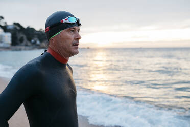 Porträt eines männlichen Schwimmers, der das Meer bei Sonnenuntergang bewundert - JRFF04972