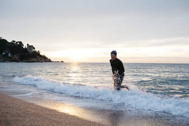 Männlicher Schwimmer verlässt das Wasser nach dem Schwimmen im Meer bei Sonnenuntergang - JRFF04973