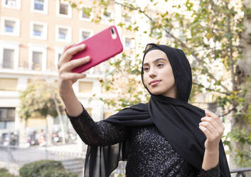 Porträt einer jungen schönen Frau mit schwarzem Hidschab, die ein Selfie mit ihrem Smartphone macht - JCCMF00468