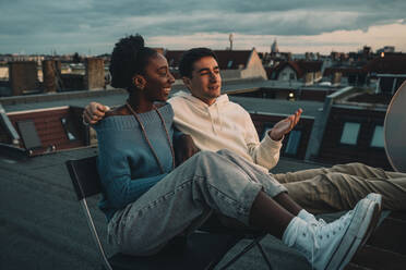 Lächelnde Frau und Mann im Gespräch auf dem Dach eines Gebäudes bei Sonnenuntergang - MASF21106
