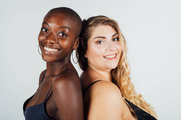 Zwei junge Frauen lächeln, Rücken an Rücken - CUF56678
