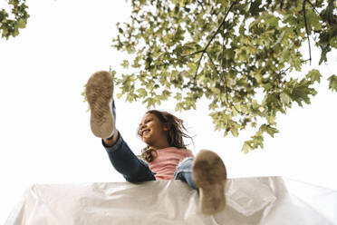 Low angle view of smiling girl sitting on table against clear sky during summer - MASF21125